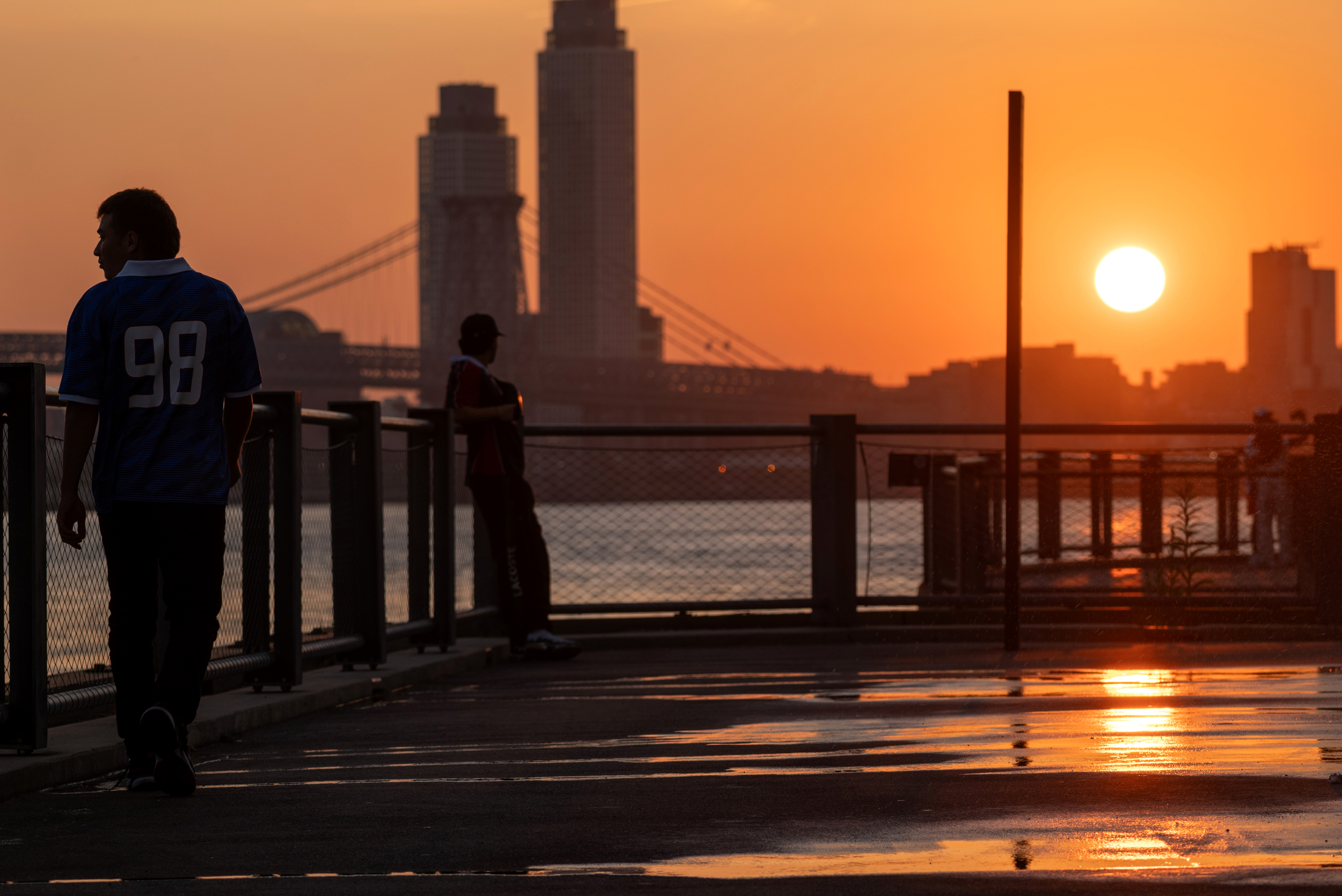 People walk along the East River in Brooklyn at sunrise on Aug. 12, as New York City experiences an air quality health advisory. Credit: Spencer Platt/Getty Images