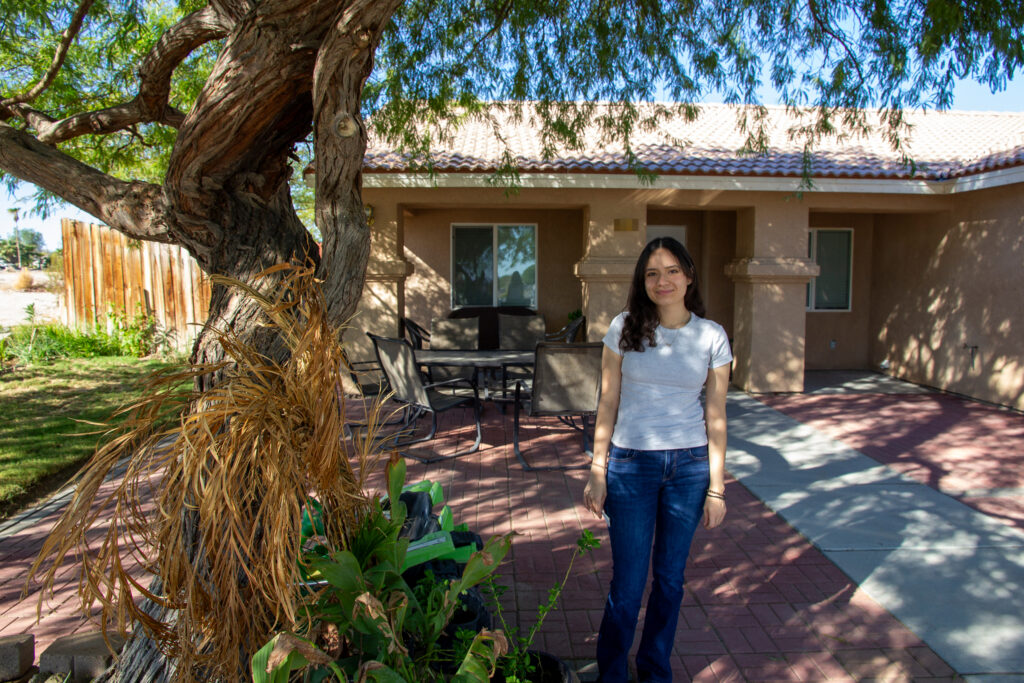 Baysi Vasquez’s daughter, Ivanna, stands in front of their home where heat pumps were installed. “All farmworkers deserve the right to affordable air conditioning,” she said. Credit: Twilight Greenaway/Inside Climate News