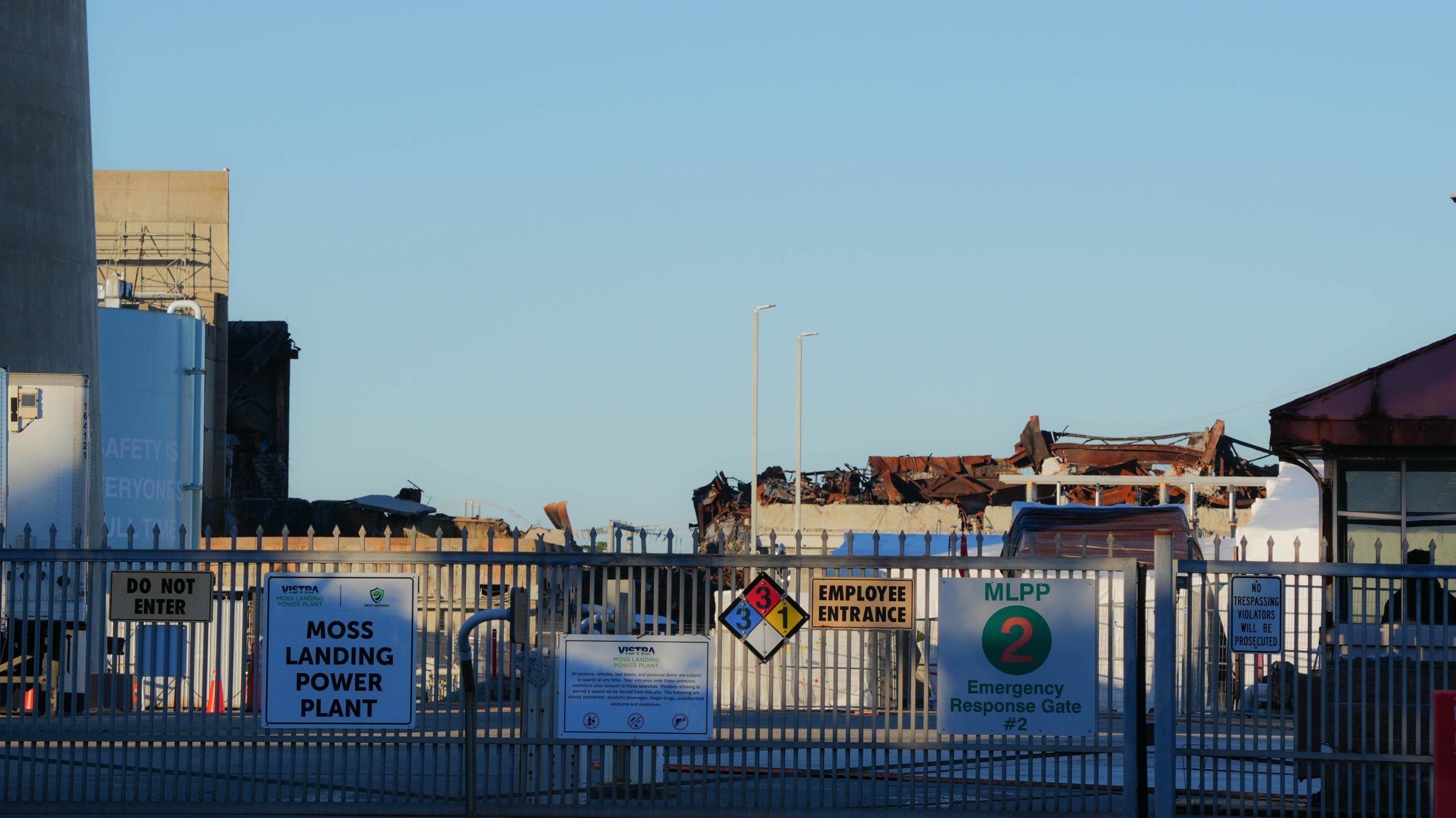 Remnants of the a massive battery fire that took place a year ago lie behind a guarded gate at Moss Landing Powder Plant. Credit: Claire Barber/Inside Climate News