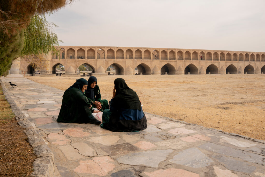 Women sit on a sidewalk along the dried-up riverbed of the Zayanderud in Isfahan, Iran, on Dec. 1, 2025. Credit: Hozi/Middle East Images/AFP via Getty Images