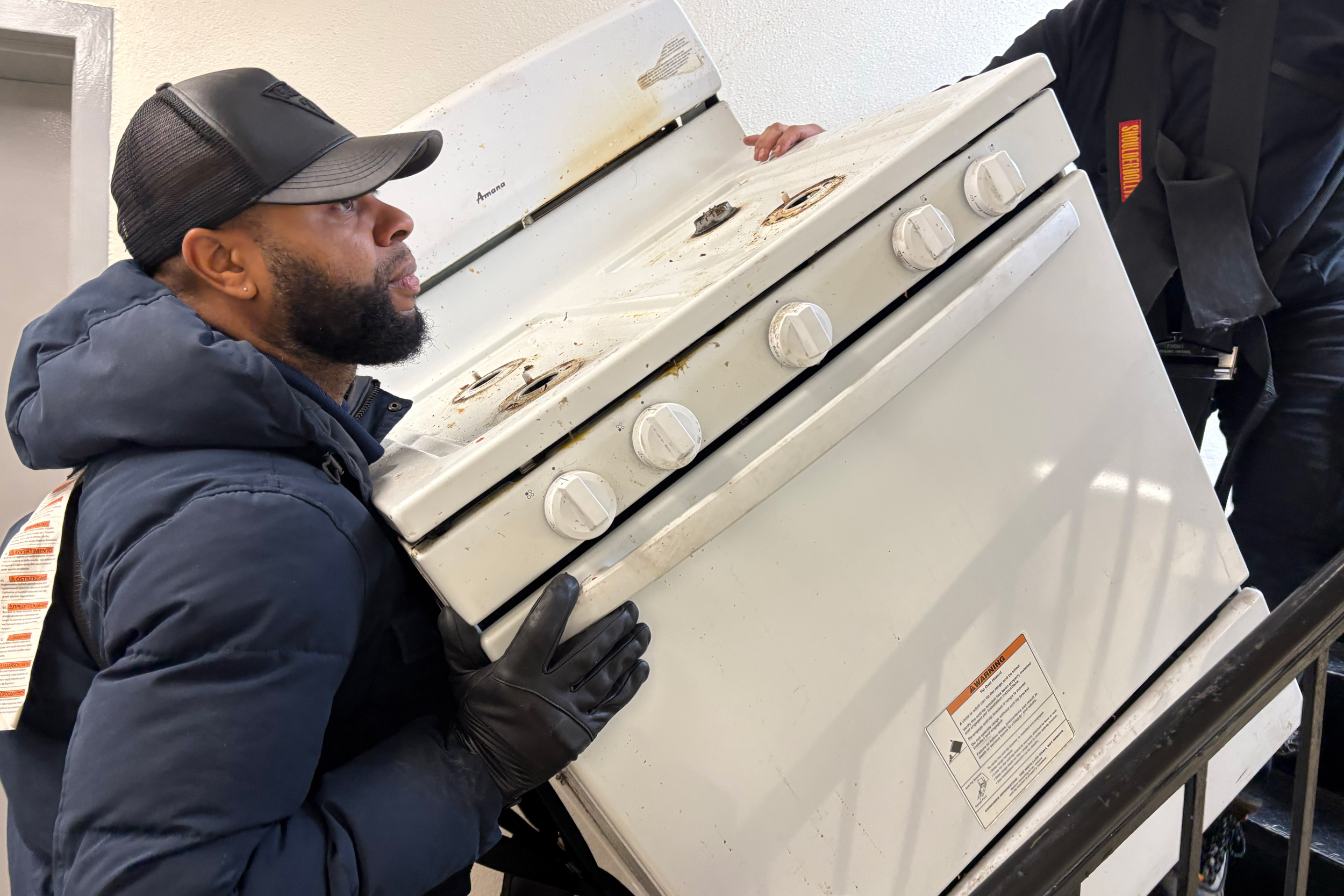 Workers remove an old stove from a Bronx apartment as part of a full-building induction stove installation in New York City. Credit: Lauren Dalban/Inside Climate News