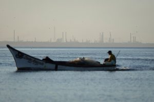 The Punta Cardon oil refinery is seen in the background of a fisherman sailing his boat from a beach in Amuay, Venezuela. Credit: Jesus Vargas/picture alliance via Getty Images