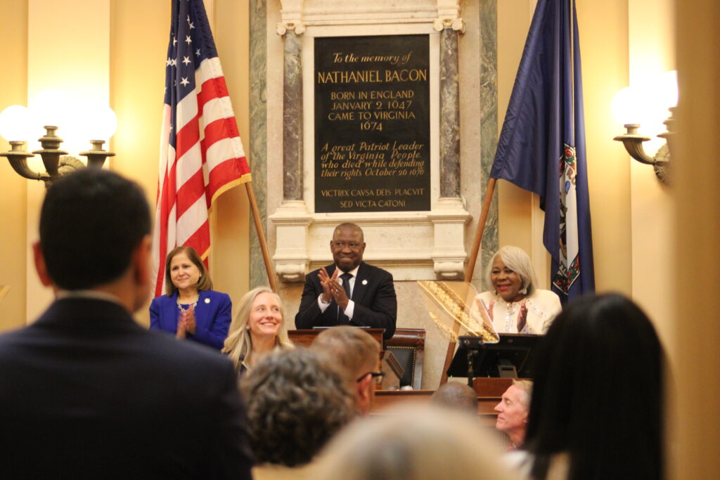 A foto está dentro de casa ao lado de bandeiras e uma placa sobre Nathaniel Bacon, que chegou à Virgínia em 1674.