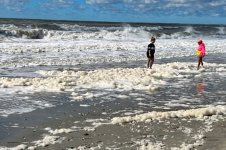 Pessoas atravessam a espuma do mar contaminada com PFAS em Holden Beach, na Carolina do Norte, em outubro de 2022. Crédito: Clean Cape Fear