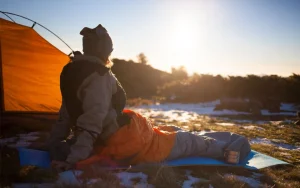 Uma menina olhando para o sol de sua barraca enquanto se aconchegava em seu saco de dormir