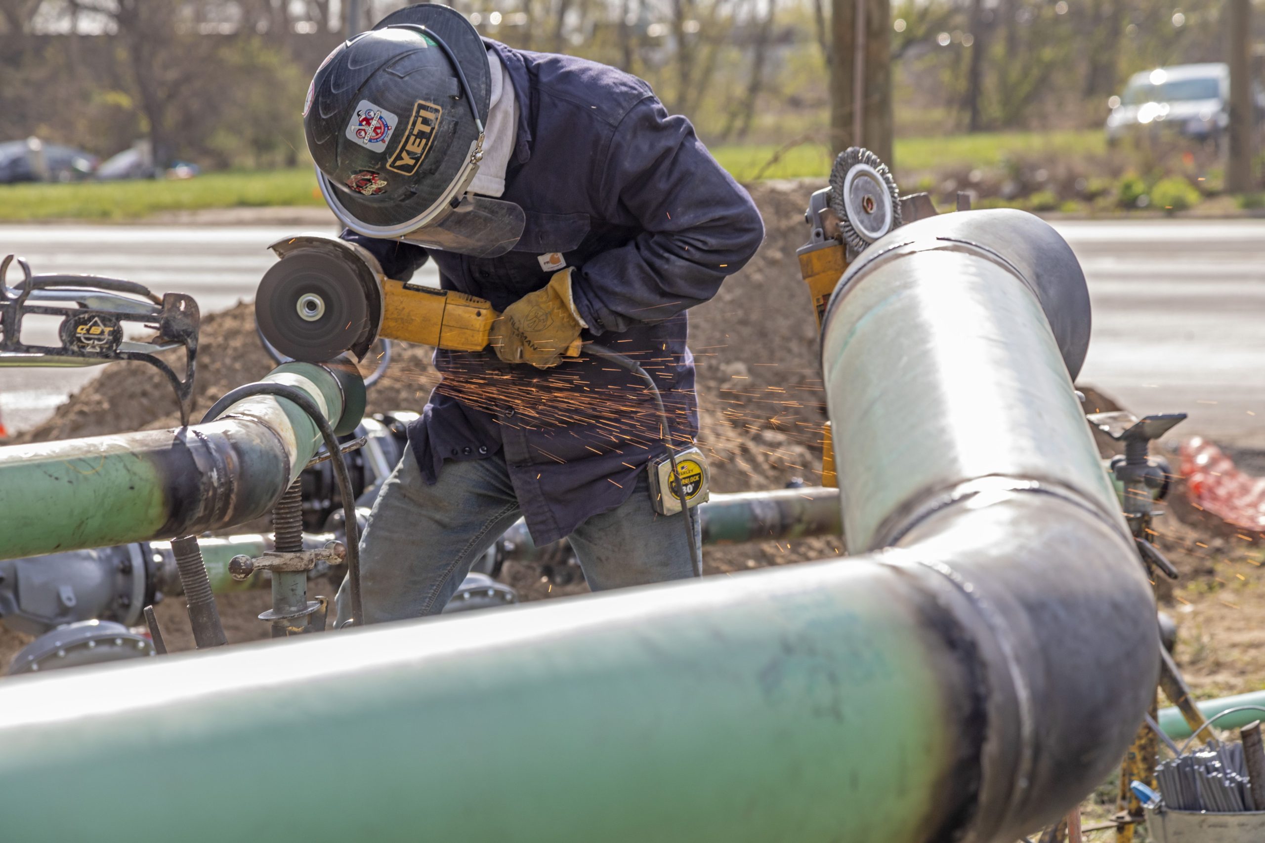 A worker in a hard hat leans over a pipe snaking over the ground.