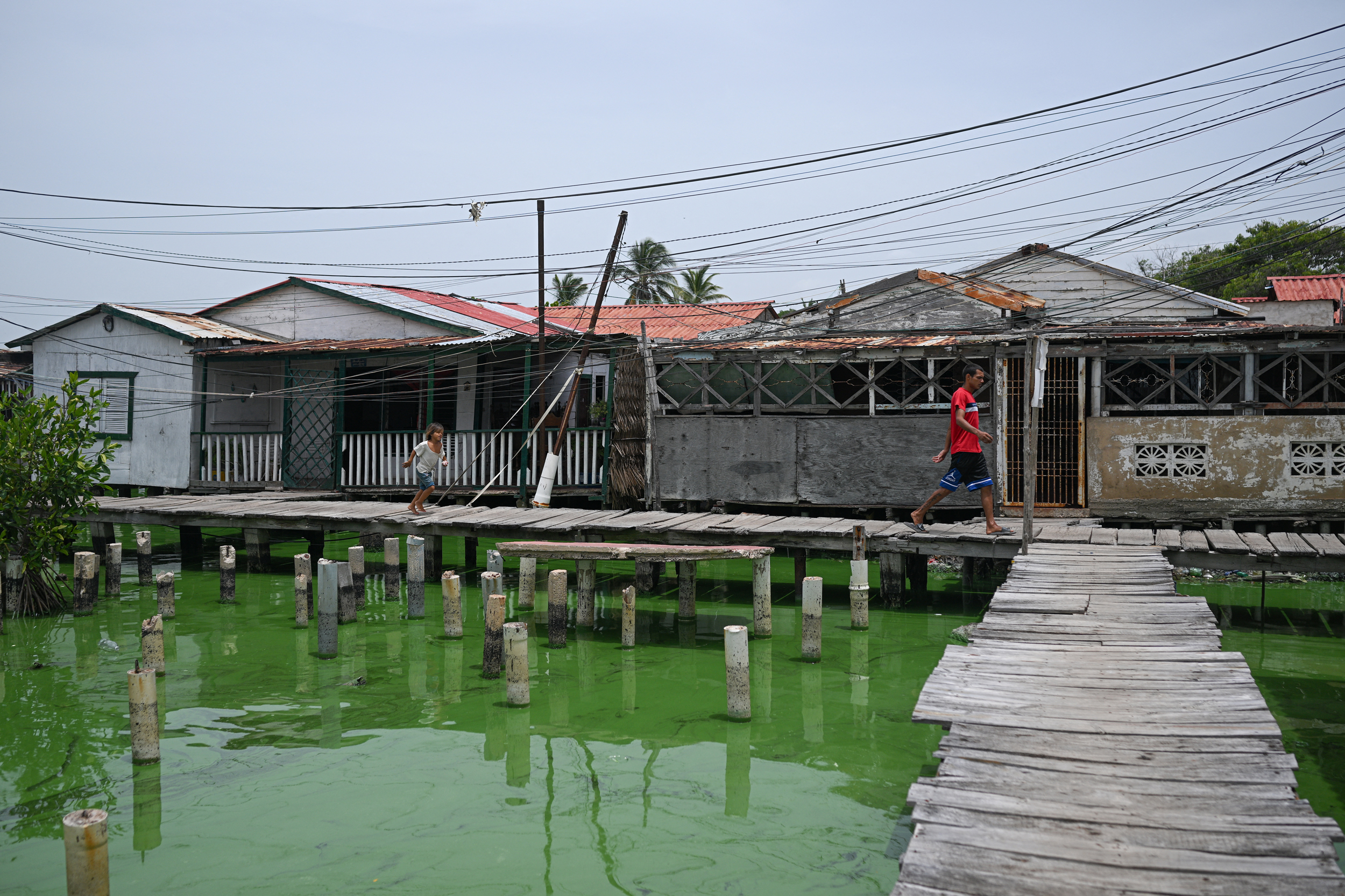 Pessoas passam por palafitas no bairro de Santa Rosa de Agua, em Maracaibo, Venezuela, enquanto uma mancha de óleo cobre as margens do Lago Maracaibo em 11 de julho de 2024. Crédito: Federico Parra/AFP via Getty Images