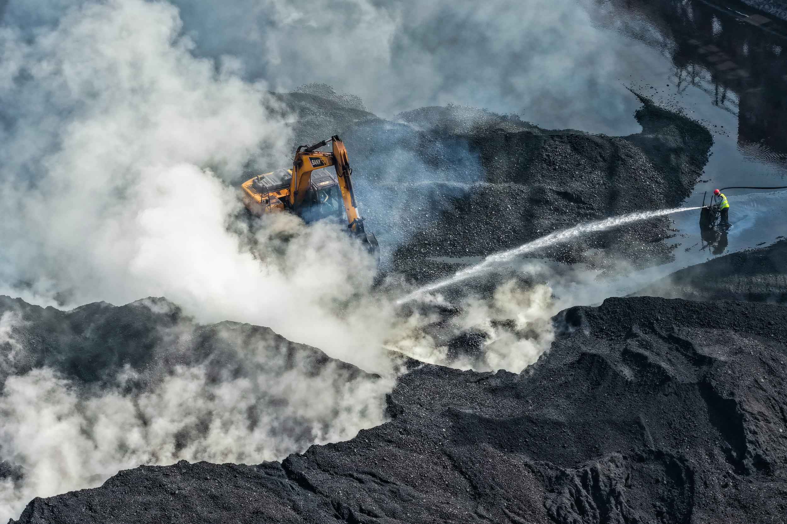Um trabalhador borrifa carvão com água em um depósito em Nanjing, China, em 31 de outubro de 2025. Crédito: CFOTO/Future Publishing via Getty Images