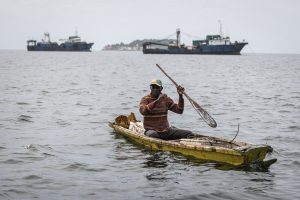 A fisherman paddles in front of commercial fishing boats off the coast of Dakar, Senegal. Credit: John Wessels/AFP via Getty Images