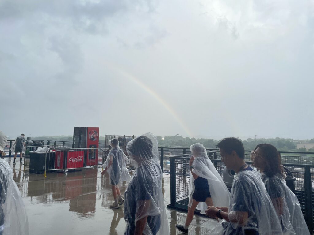 Pessoas com óculos de sol transparentes andam em primeiro plano, com o arco-íris ao fundo