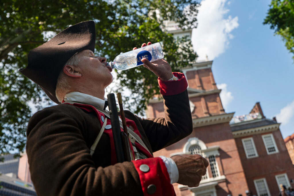 A Revolutionary War reenactor drinks water in the shade near Independence Hall during high temperatures on July 3 in Philadelphia. Credit: Al Drago/Getty Images