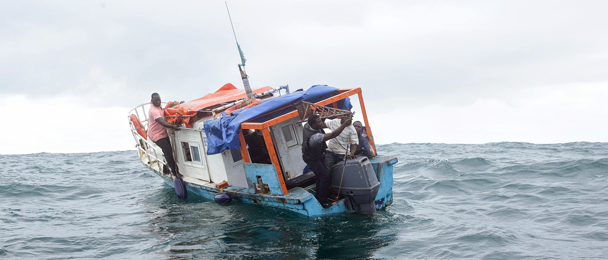 Gérard Zinzindohoué e a sua equipa preparam-se para implantar um scanner sonar na popa de um barco de pesca local. Crédito: Ghislain Adjahouisso