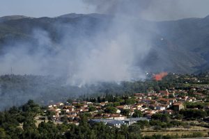 Thick smoke rises from a mountain range overlooking the community of Vinca, France, tucked between trees.