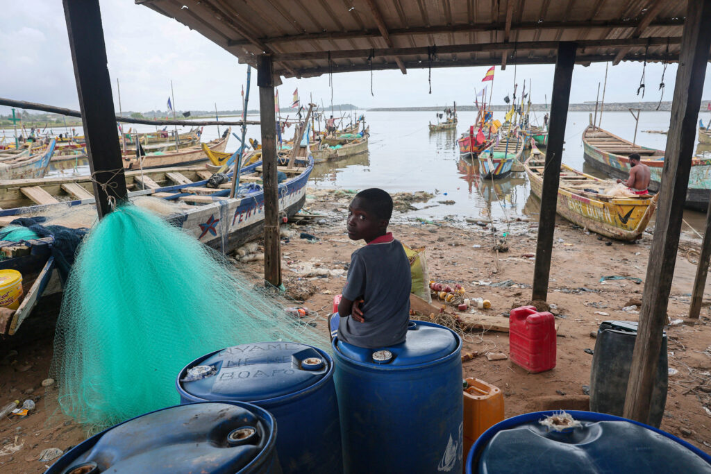 A boy sits near fishing boats in Adwoa, Ghana, on June 23. Credit: Nipah Dennis/AFP via Getty Images