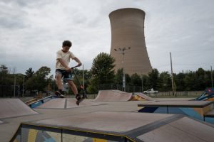 A child plays on a scooter in the park, with the cooling tower looming in the background.