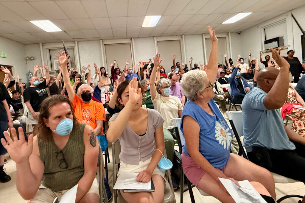 Residents raise their hands after being asked if the Maryland Department of the Environment should deny WIN Waste’s permit renewal during an Oct. 1 public hearing in Curtis Bay. Credit: Aman Azhar/Inside Climate News