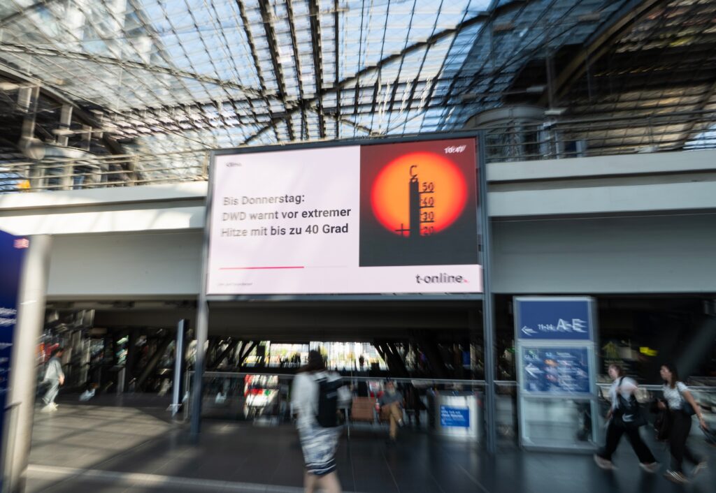 Passengers walk past a heat-warning display at the main train station in Berlin, Germany