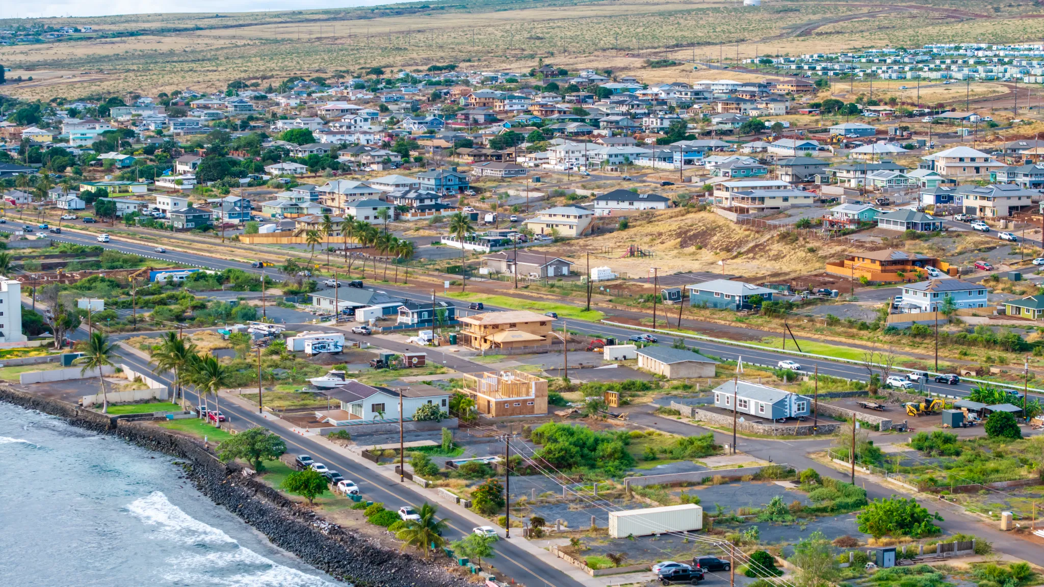 An aerial photo shows a portion of Lahaina, Hawaii, near the water. Properties are a mix of homes, houses under construction and empty lots.